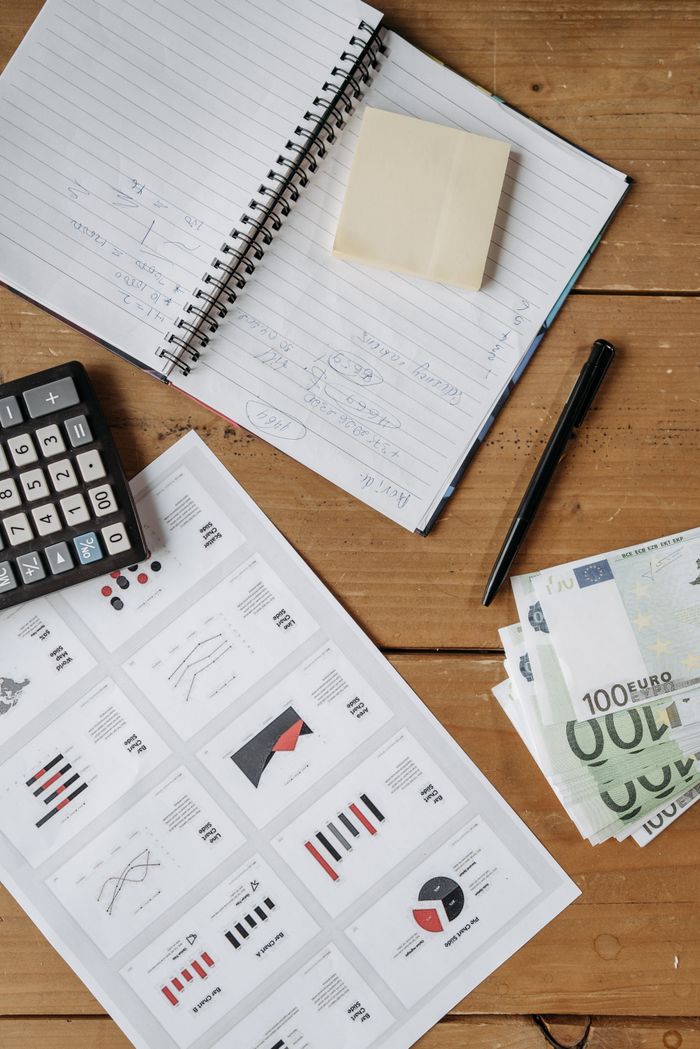 Home High-angle view of a financial workspace with charts, Euro bills, calculator, and notebook on a wooden desk.