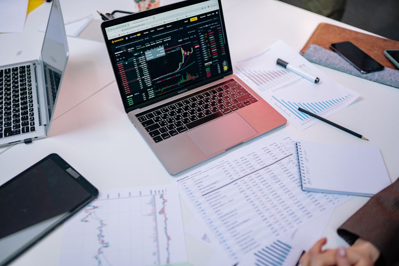 Home Laptops on a desk displaying stock market charts and financial documents.