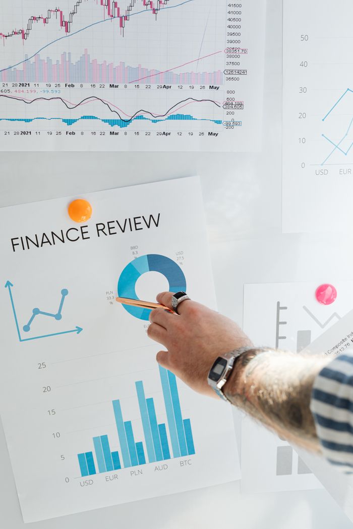 Home Hand pointing at a financial chart on a wall, illustrating data analysis and review.